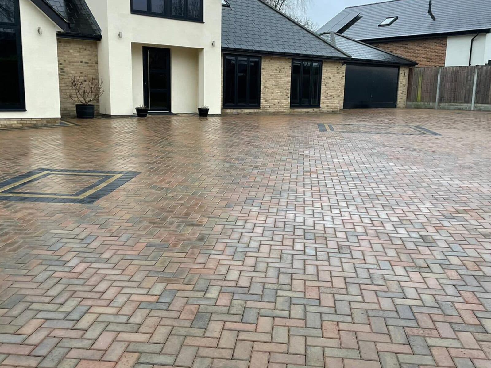 Brindle block paved driveway laid in herringbone, with charcoal and buff inset squares, in front of a large rendered house