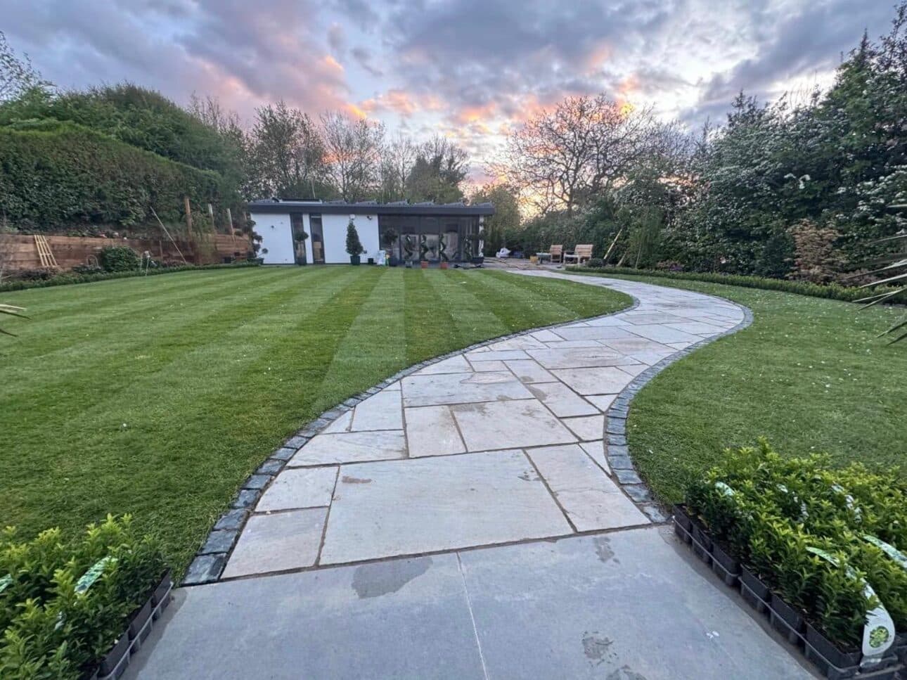Curved natural stone path running through a striped lawn, edged with planting