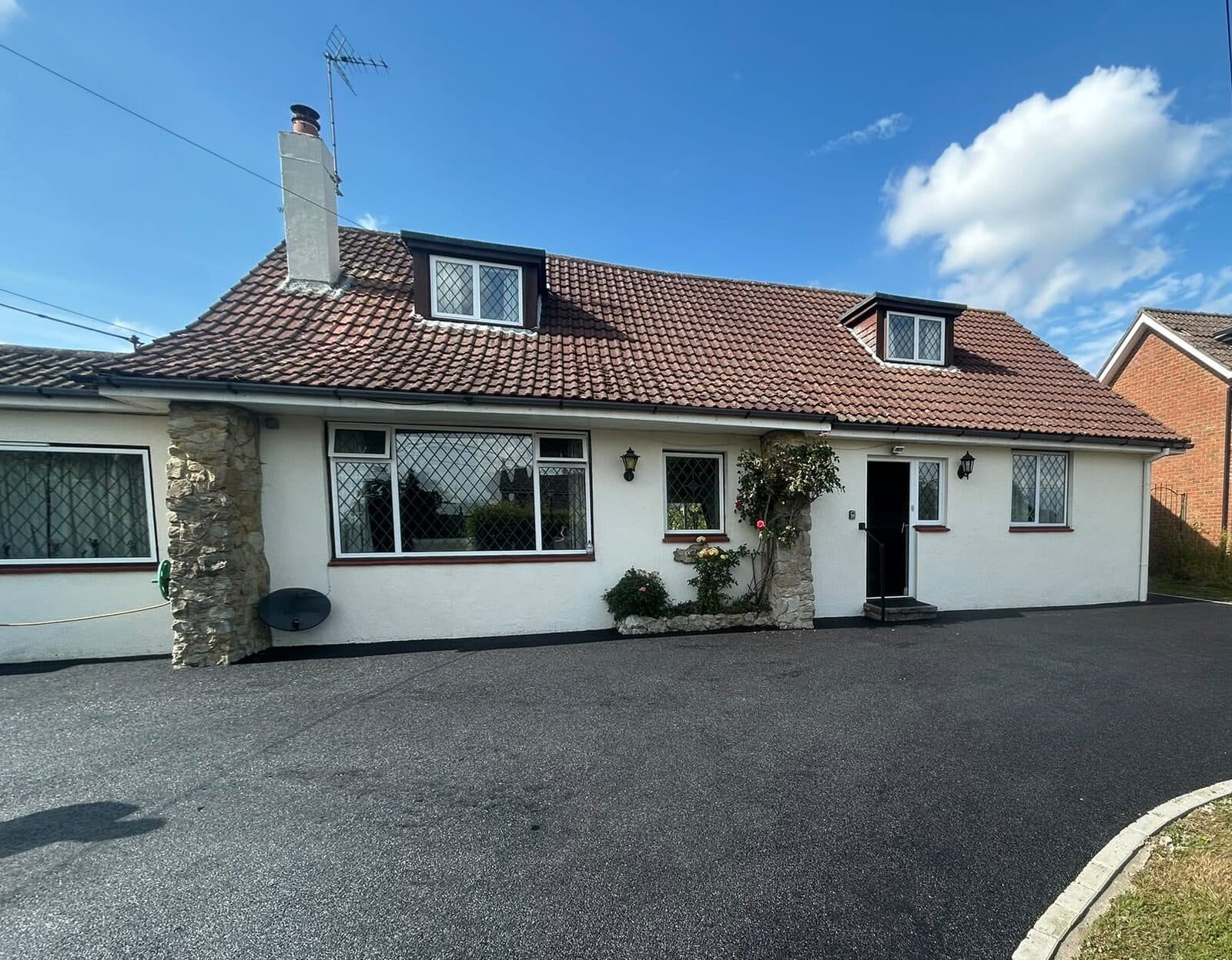 Freshly laid black tarmac driveway with a light kerb edge, in front of a white bungalow