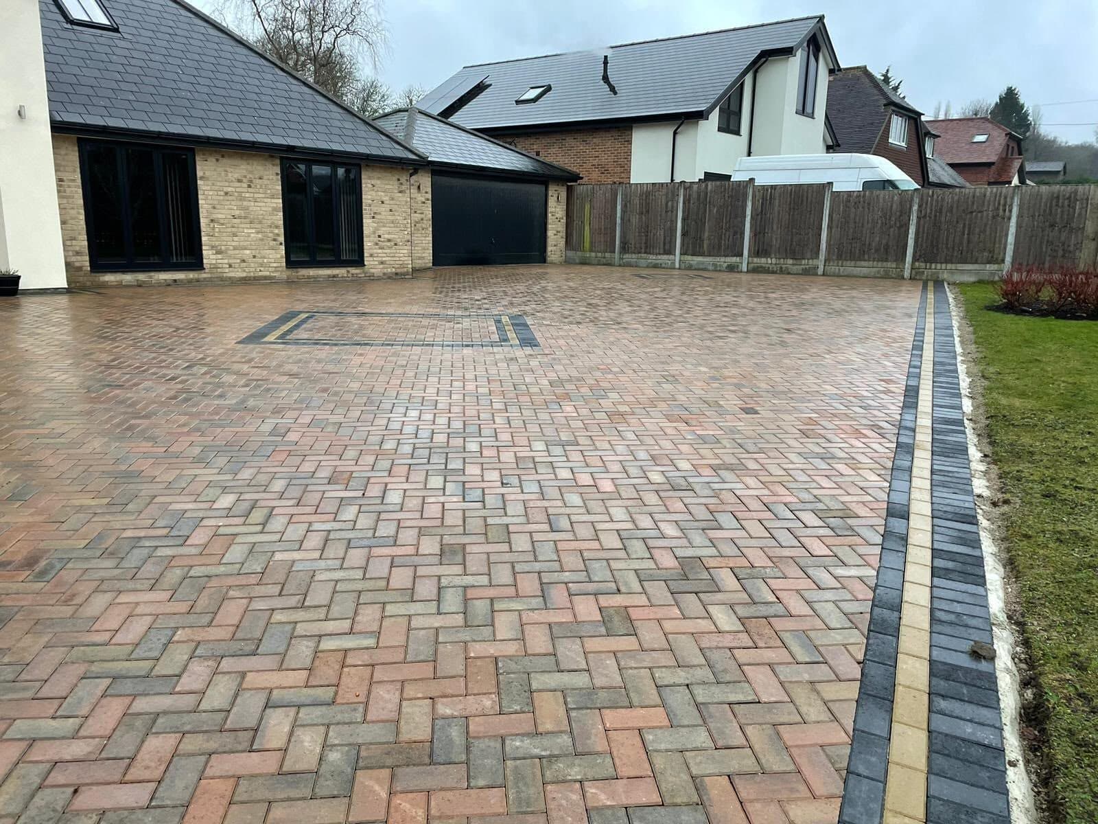 Brindle herringbone block paved driveway with a charcoal soldier-course border and a picture-frame inset beside a modern house and garage