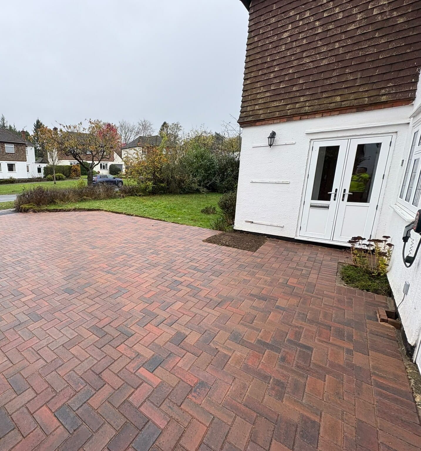 Red and charcoal brindle herringbone block paving in front of a white rendered house with a tile-hung gable
