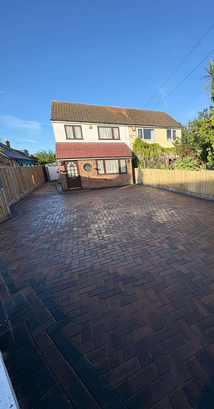 Large sunlit herringbone block paved driveway with a contrasting border in front of a detached house