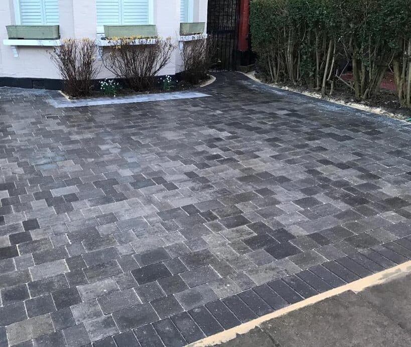 Tumbled charcoal block paved driveway edged with a curved planted border