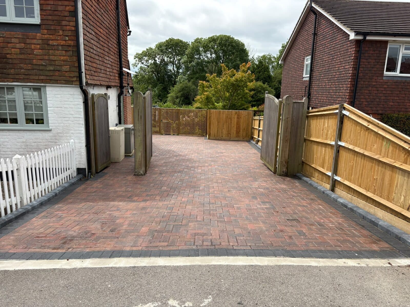 New closeboard fencing, lattice-topped panels and tall timber gates around a red brindle herringbone block paved driveway