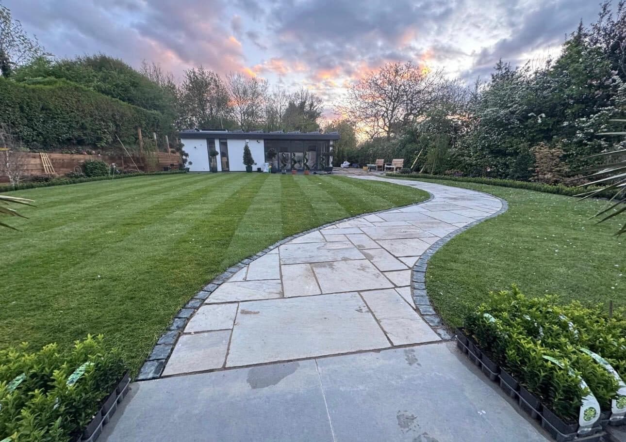 Curved natural stone path running through a neatly striped lawn, edged with low box hedging