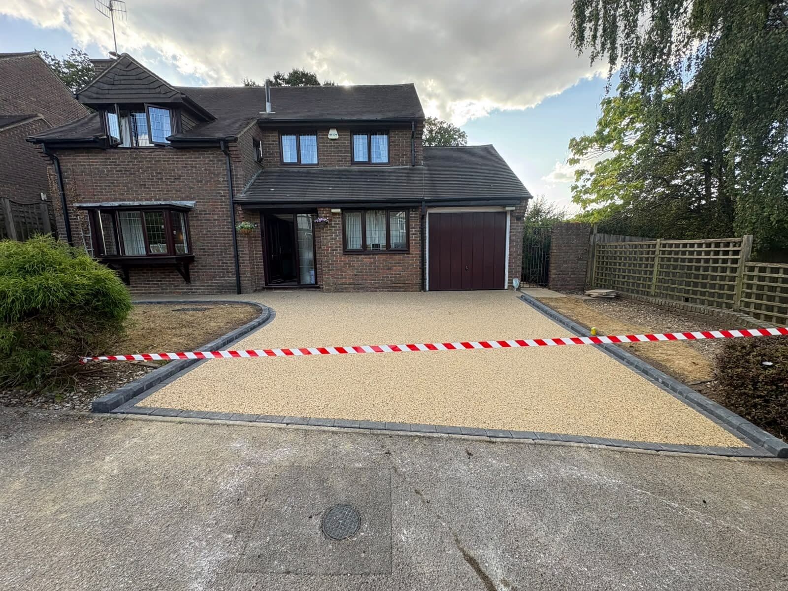 Newly laid gold resin-bound driveway with a charcoal block border in front of a detached brick house