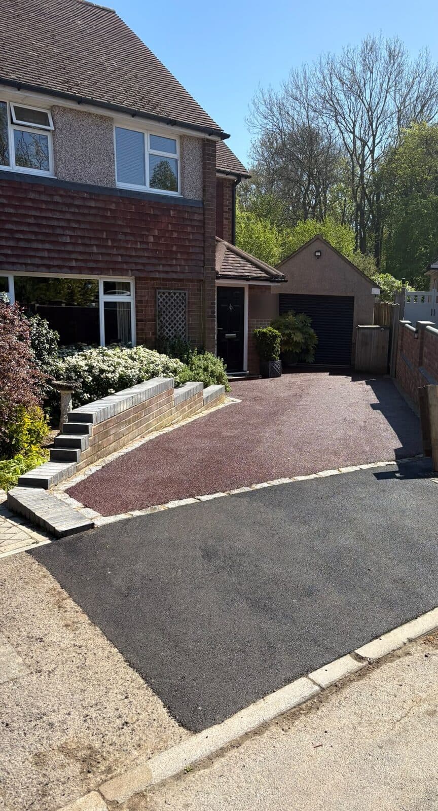 Red resin-bound driveway running from the front door to a black tarmac apron at the road