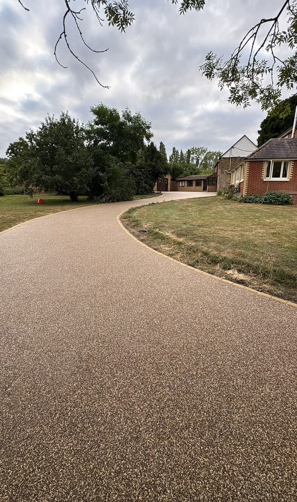 Long gold resin-bound driveway sweeping in a curve past a lawn