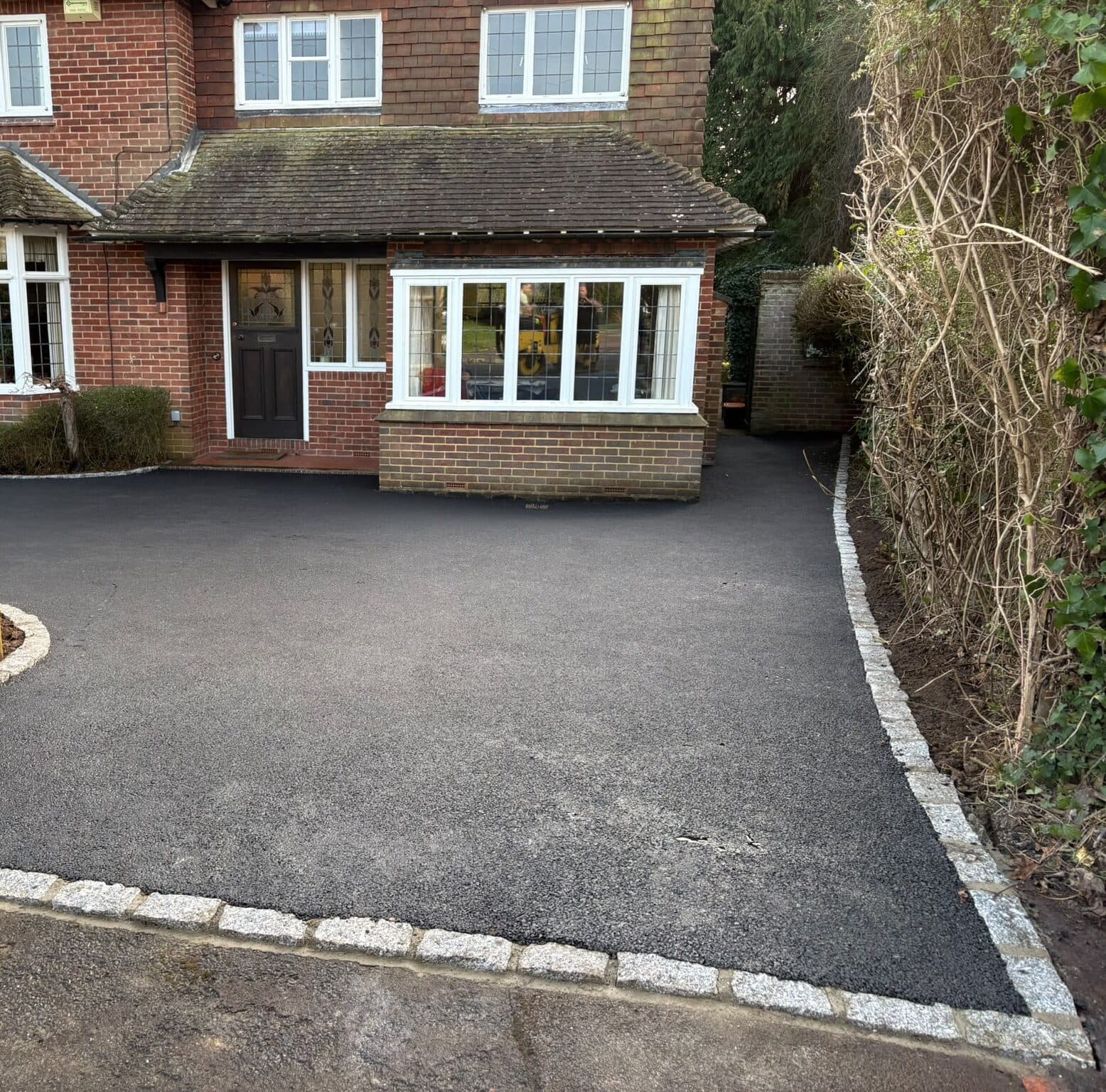 Black tarmac driveway edged with light granite setts in front of a detached house